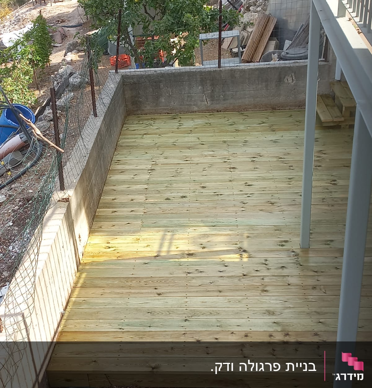 דק עץ חדש בגינה עם קיר בטון מסביב